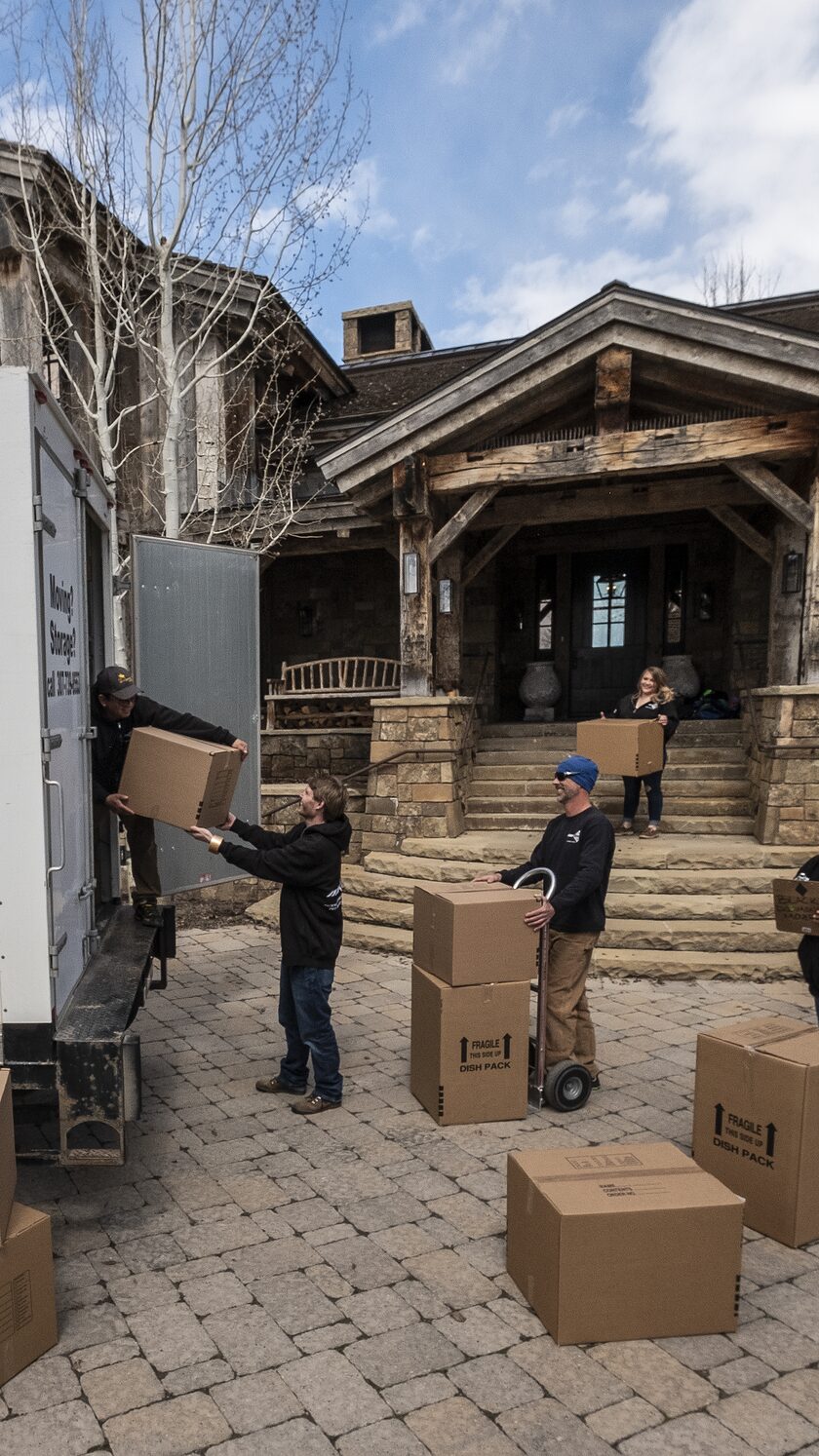 A moving crew carrying boxes outside a mountain home.